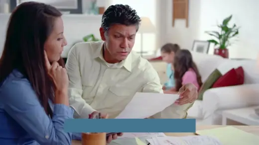 A concerned man reviews documents with a woman in a light-filled living room.