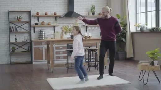 A man and girl dance on a rug in a kitchen.