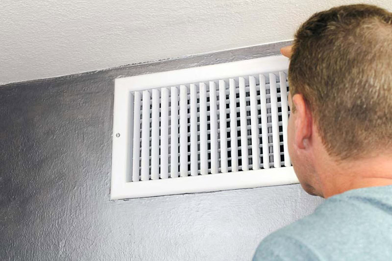 man in blue shirt looking at white wall air vent