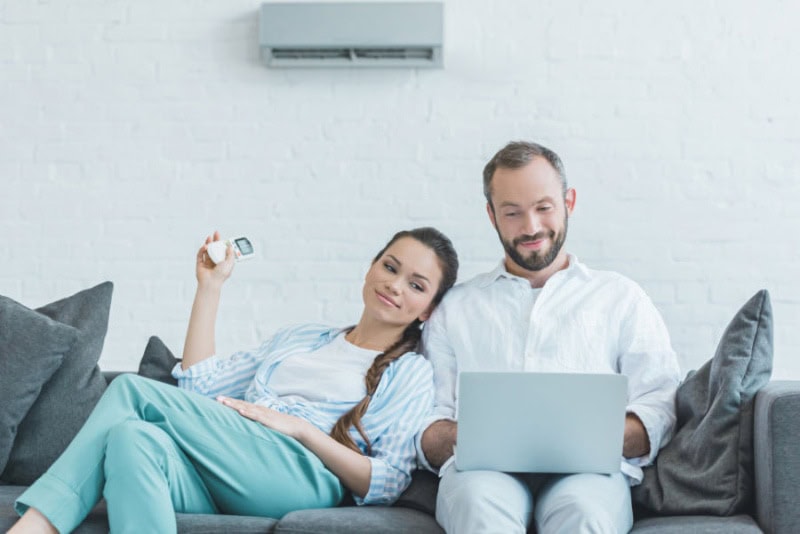 Couple sitting on a couch turning on a ductless unit with a remote.