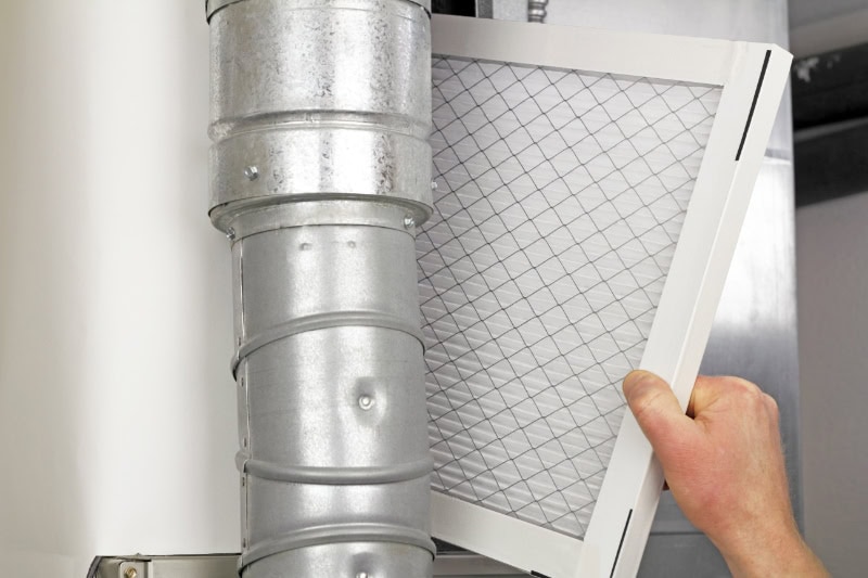 How Can I Make My Furnace Last Longer? - Male arm and hand replacing disposable air filter in residential air furnace.